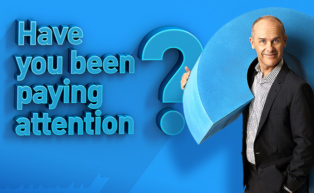 Tom Gleisner poses holding a question mark next to the Have You Been Paying Attention? logo