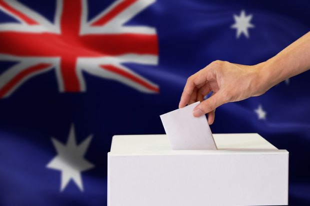 A white hand places a ballot paper into a ballot box with the Australian flag in the background